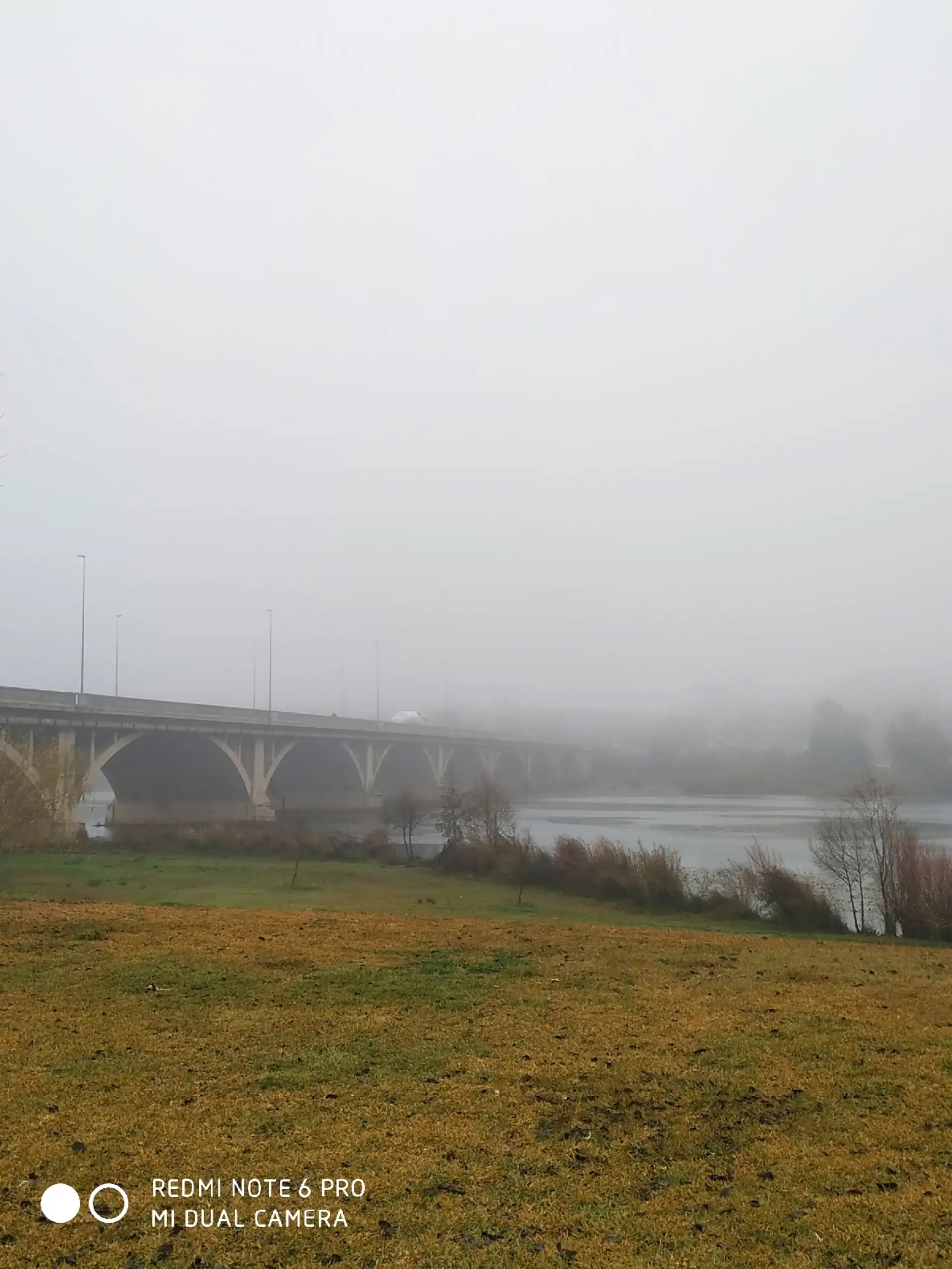 Puente sobre un río envuelto en niebla, con el paisaje difuminado al fondo