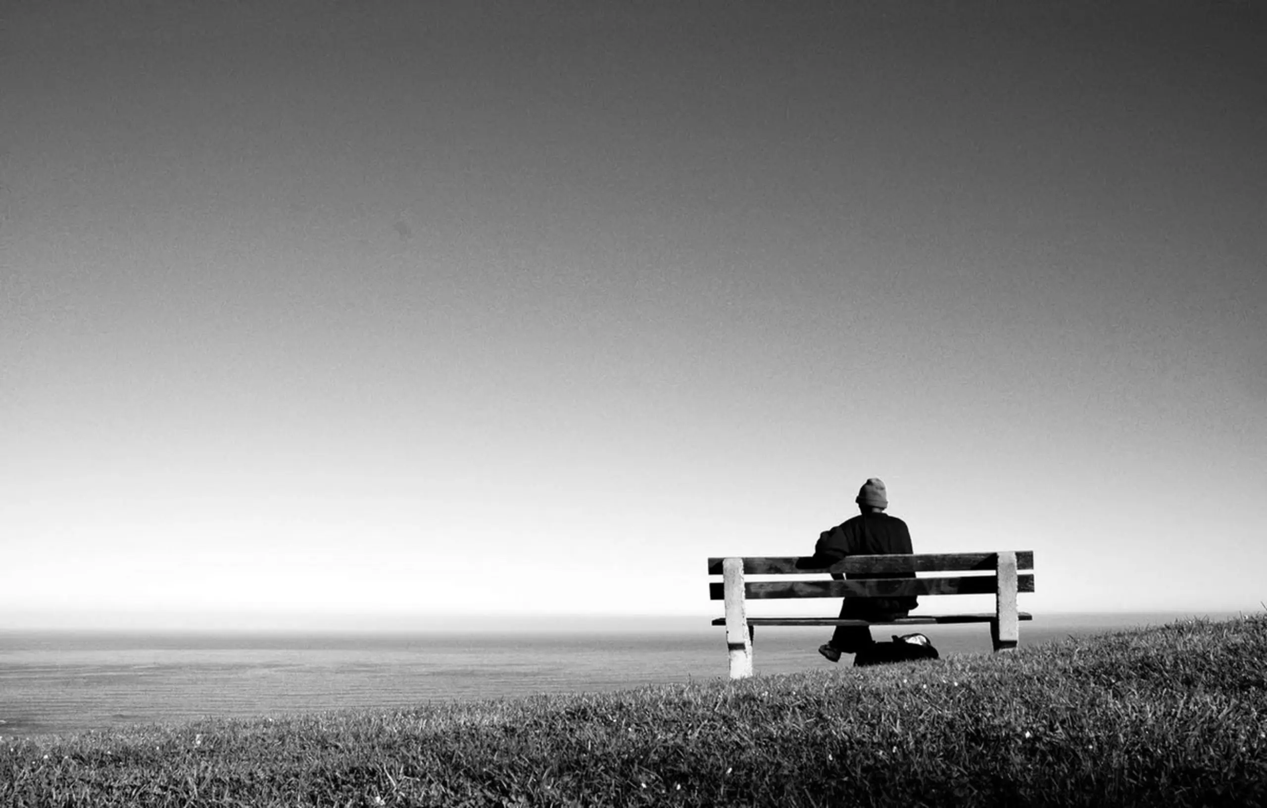 Persona sentada de espaldas en un banco frente al mar, fotografía en blanco y negro