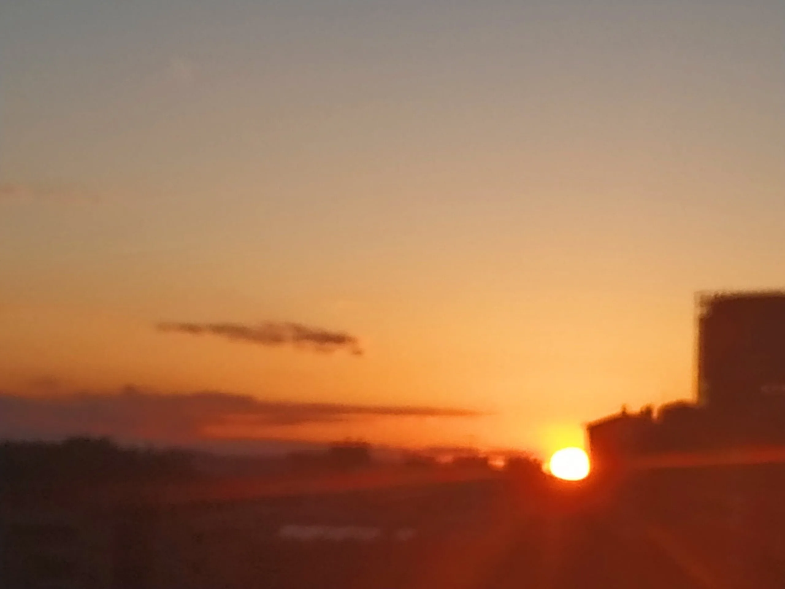 Puesta de sol anaranjada con la silueta de un edificio en primer plano