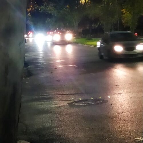 Calle de noche con coches circulando y sus faros iluminando el asfalto mojado