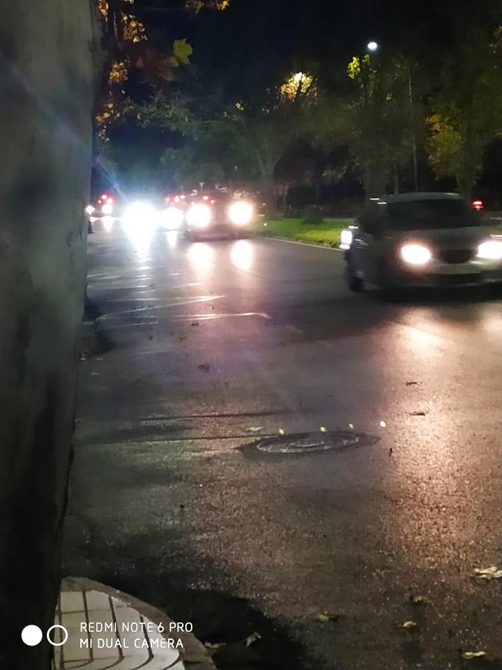 Calle de noche con coches circulando y sus faros iluminando el asfalto mojado