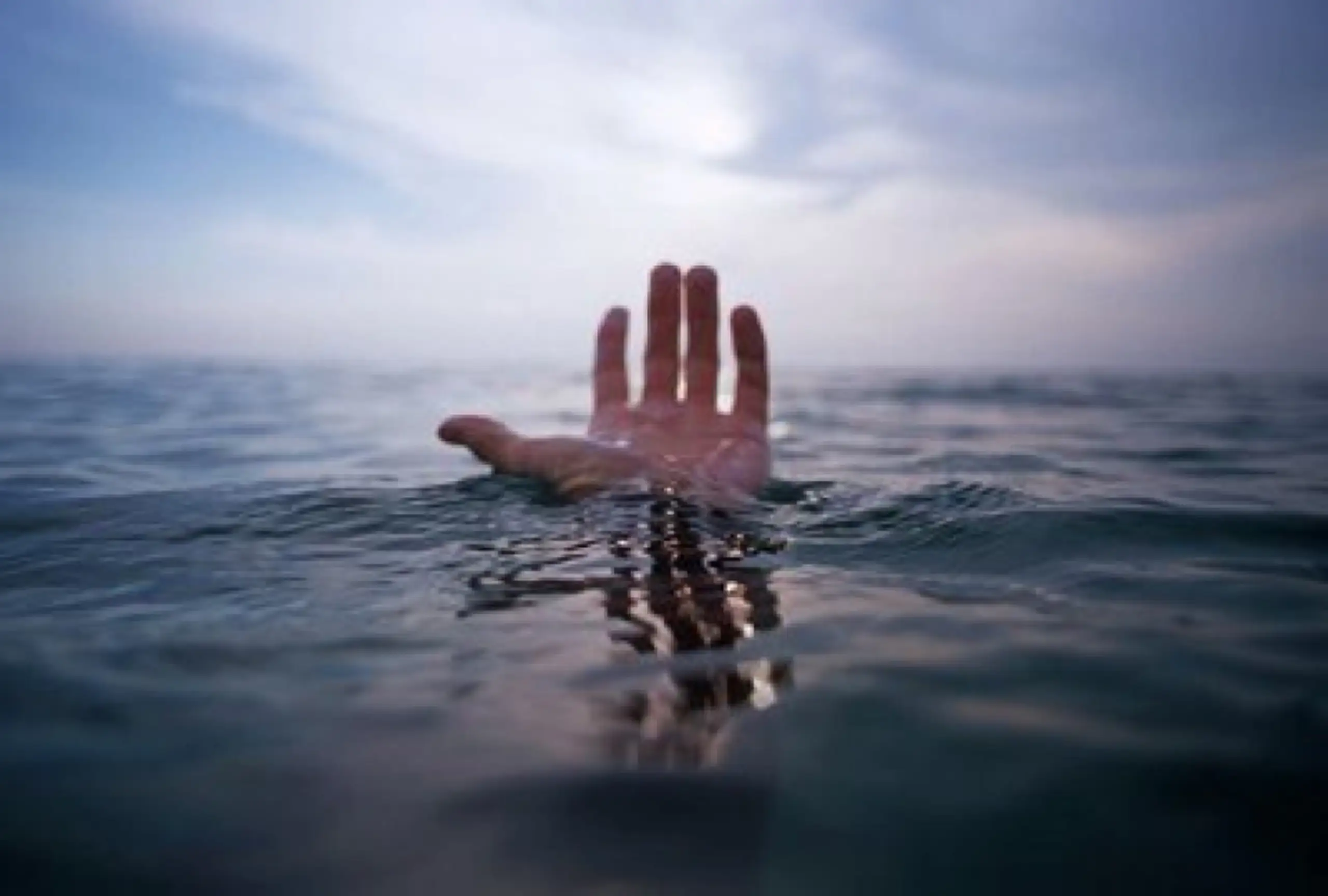 Mano emergiendo del mar hacia el cielo, con el sol difuminado entre nubes