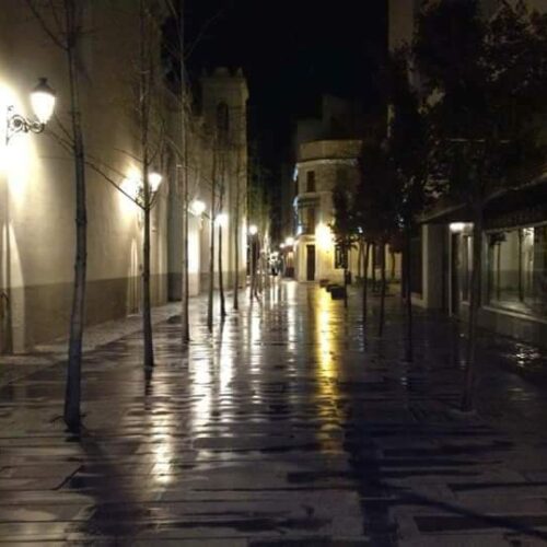 Calle empedrada de noche, mojada por la lluvia, con farolas reflejadas en el suelo