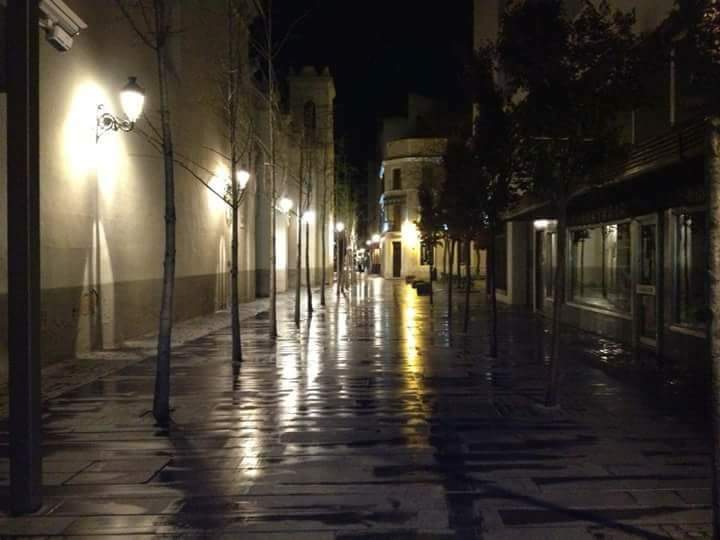 Calle empedrada de noche, mojada por la lluvia, con farolas reflejadas en el suelo