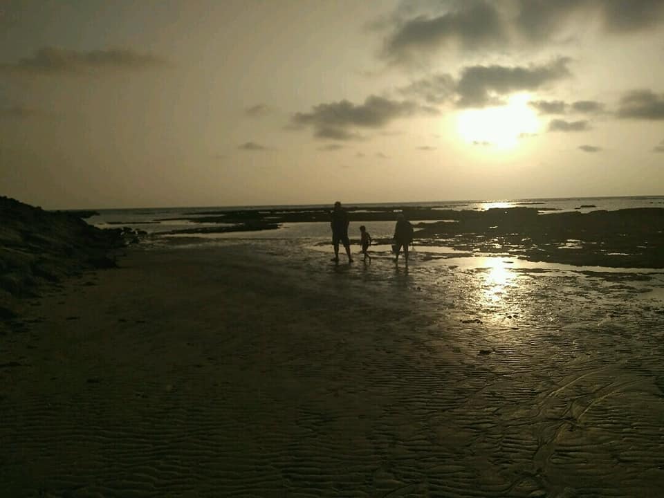 Tres siluetas caminando por la orilla del mar al atardecer, con el sol reflejado en el agua