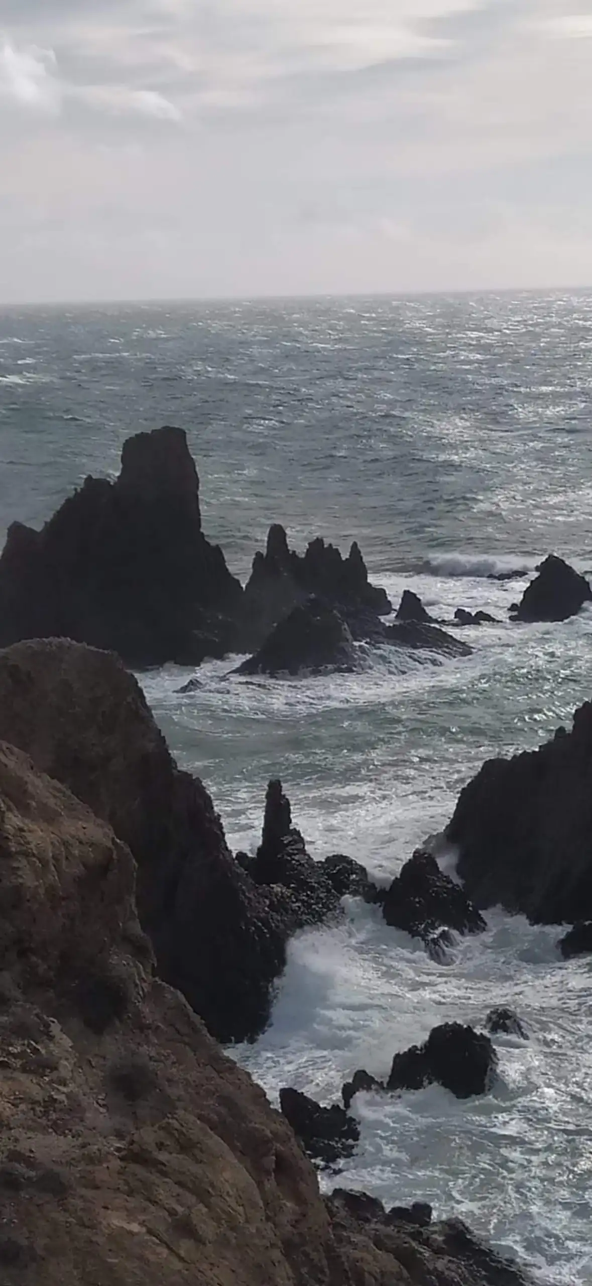 Rocas negras y afiladas en la costa con el mar rompiendo entre ellas