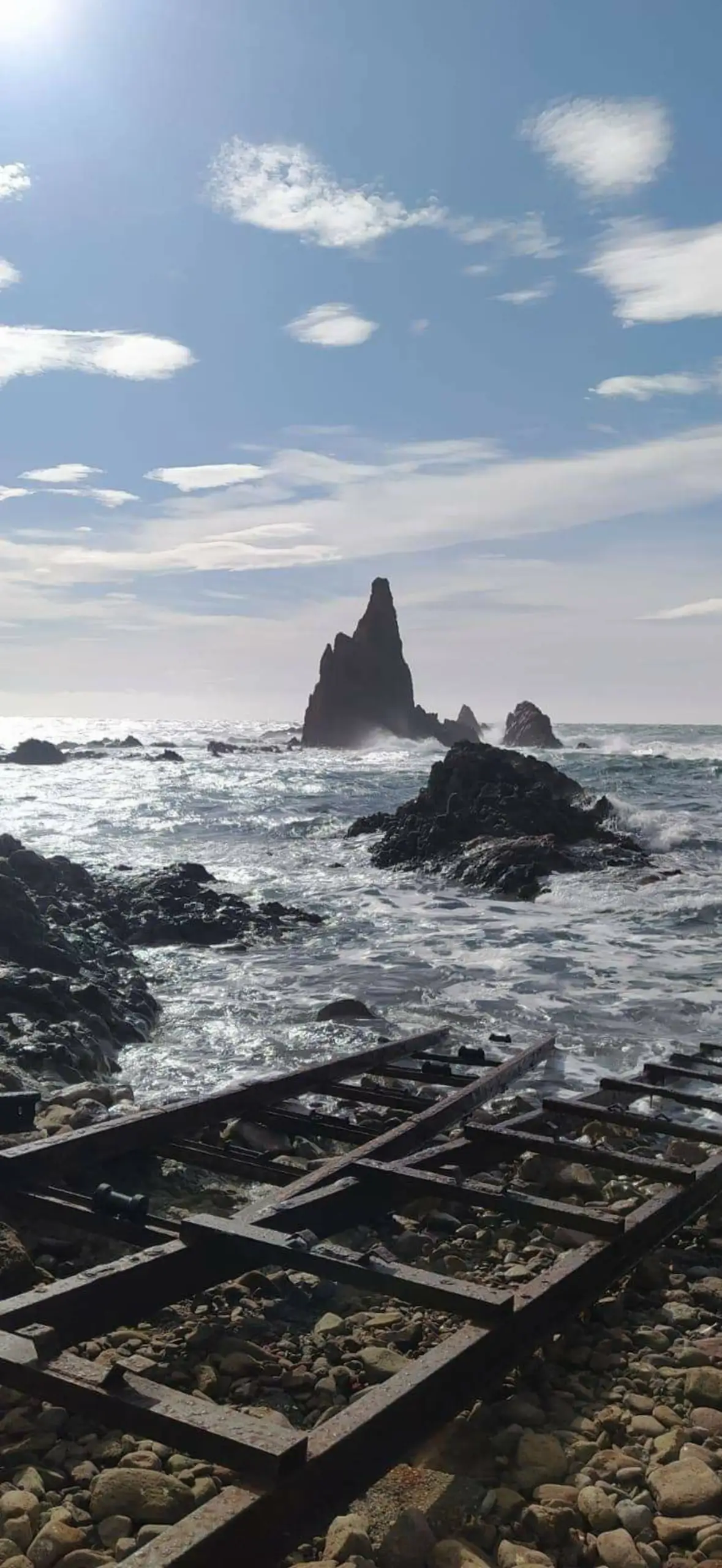 Formación rocosa en el mar con restos de una estructura metálica oxidada en la orilla