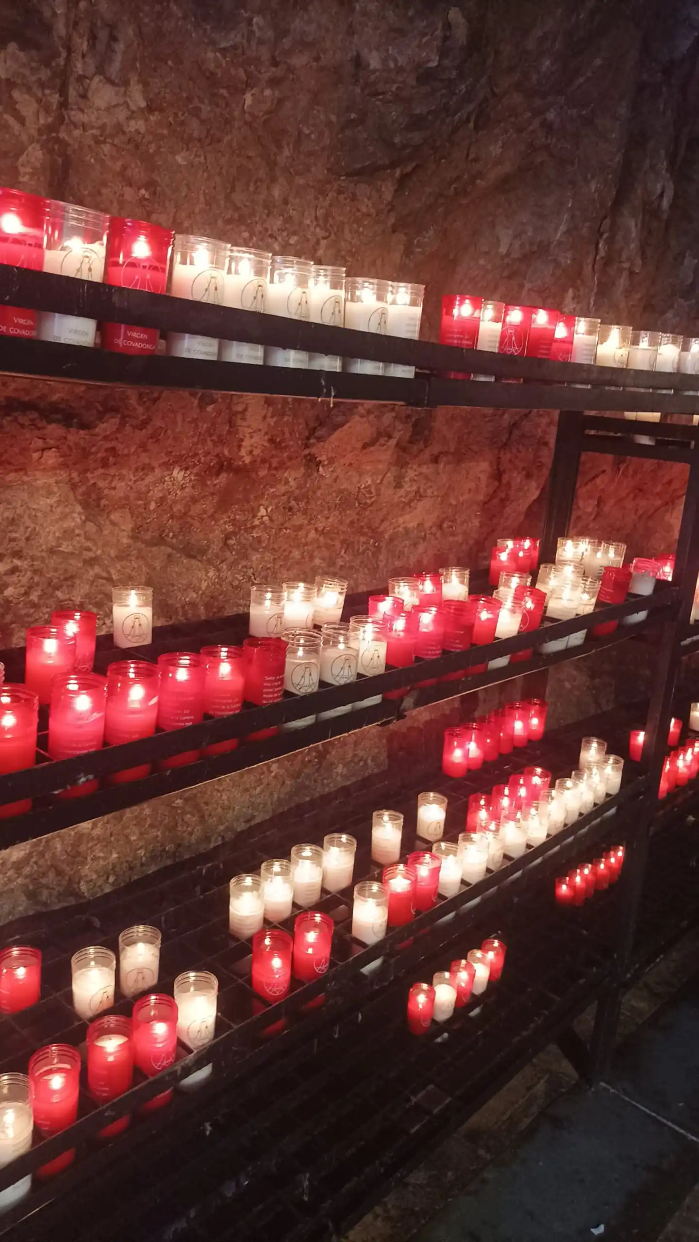 Velas votivas rojas y blancas encendidas en un santuario, dedicadas a la Virgen de Covadonga