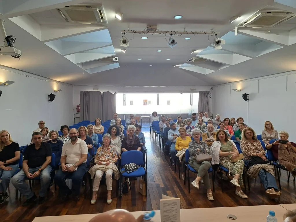 Público asistiendo a una presentación de libro en una sala con proyectores en el techo